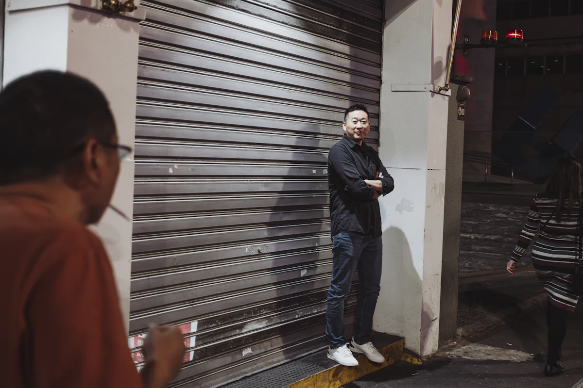 Pria berdiri di samping rolling door toko yang sudah ditutup