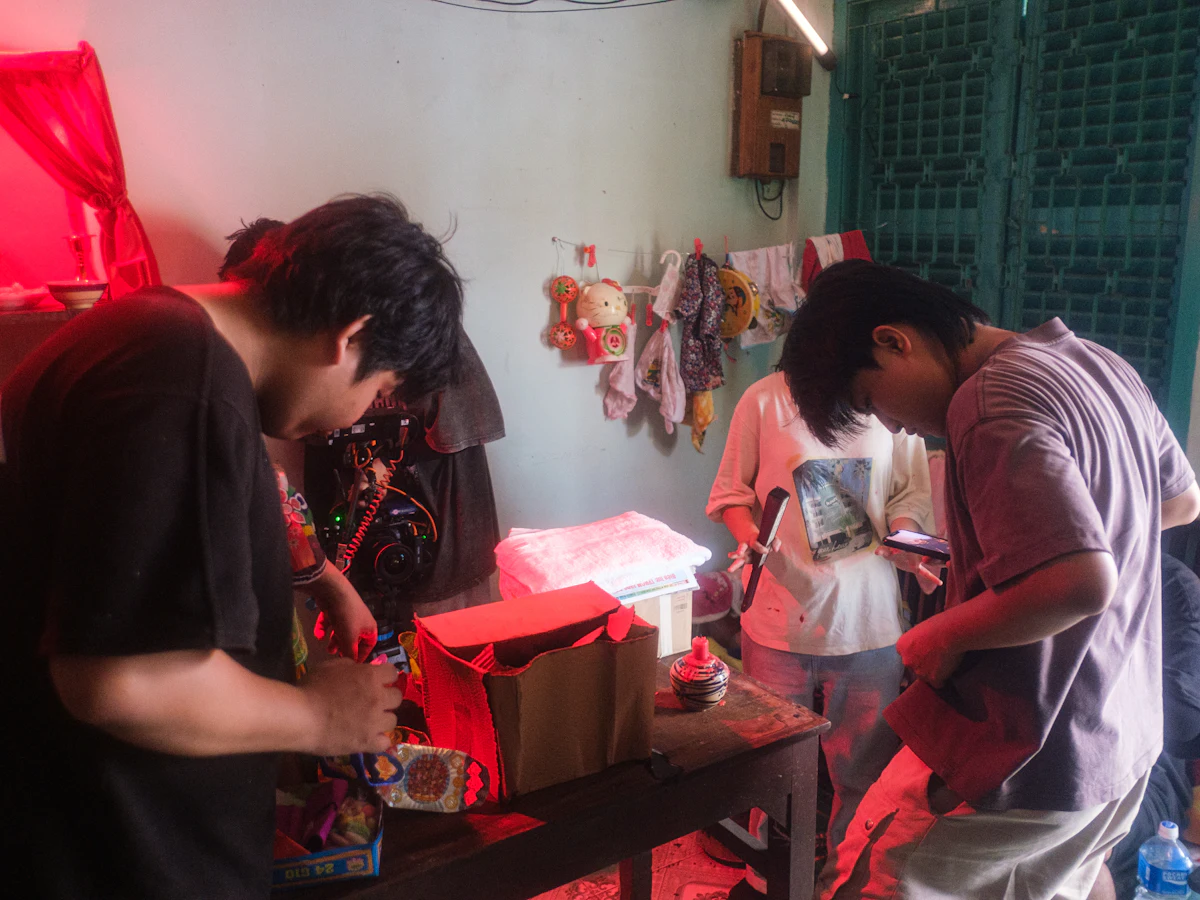 Pegawai menyortir dan mengemas paket berwarna-warni di meja panjang usaha rumahan; dua orang memegang ponsel sambil bekerja