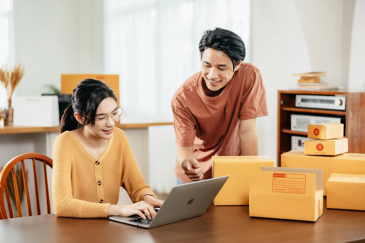 Dua orang berbagi satu meja kerja sambil melihat layar laptop yang sama
