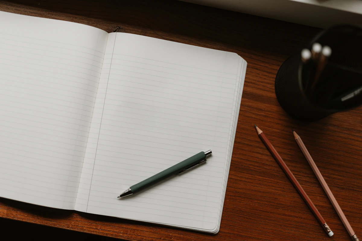 Buku catatan terbuka dengan pulpen di atas meja kayu