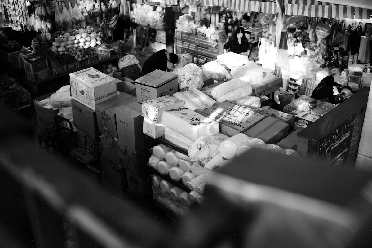 Tumpukan kardus dan wadah plastik menumpuk di sudut kios yang sempit