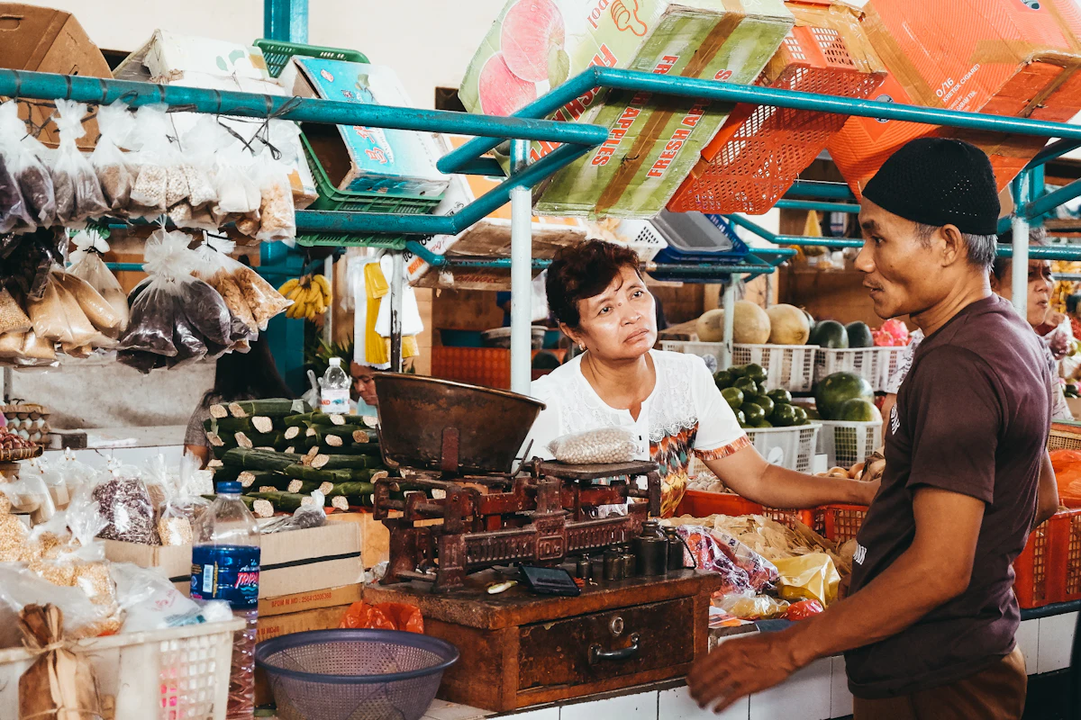 Seorang perempuan menjual barang dagangannya di sebuah toko kecil di Indonesia, dagangan tertata di meja depan.