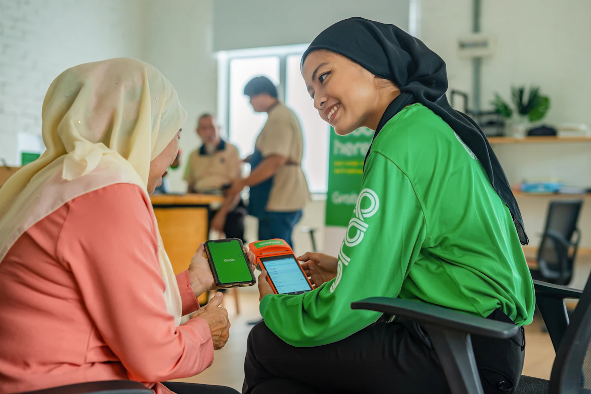 Seorang perempuan berjilbab menyerahkan ponsel kepada rekan kerjanya di dalam toko