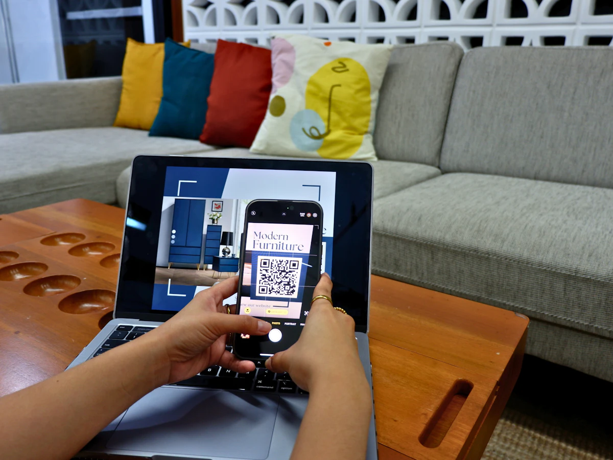 Seseorang memakai laptop yang menampilkan kode QR di layarnya sambil memegang ponsel