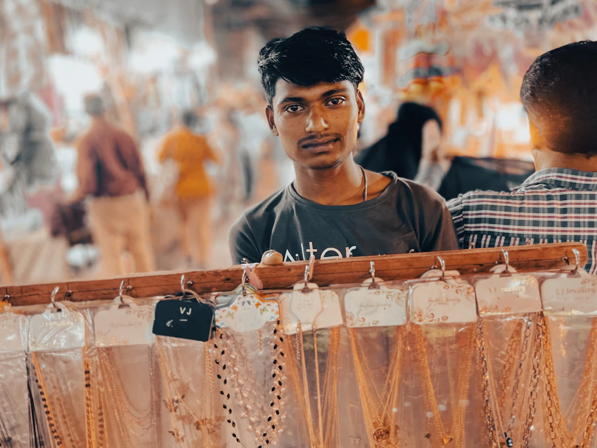 Penjual berdiri di balik etalase barang yang setiap itemnya menggantung dengan kartu label harga