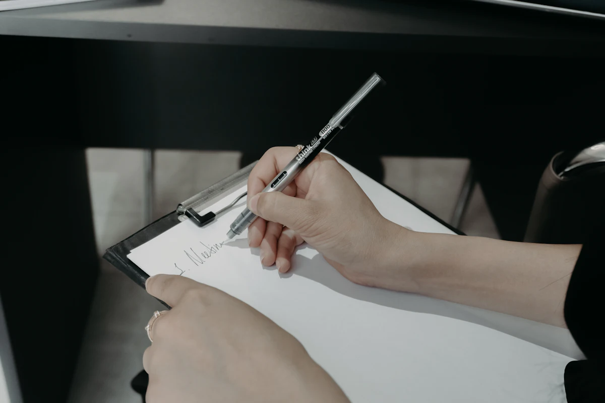 Tangan menulis dengan pulpen di atas papan klip