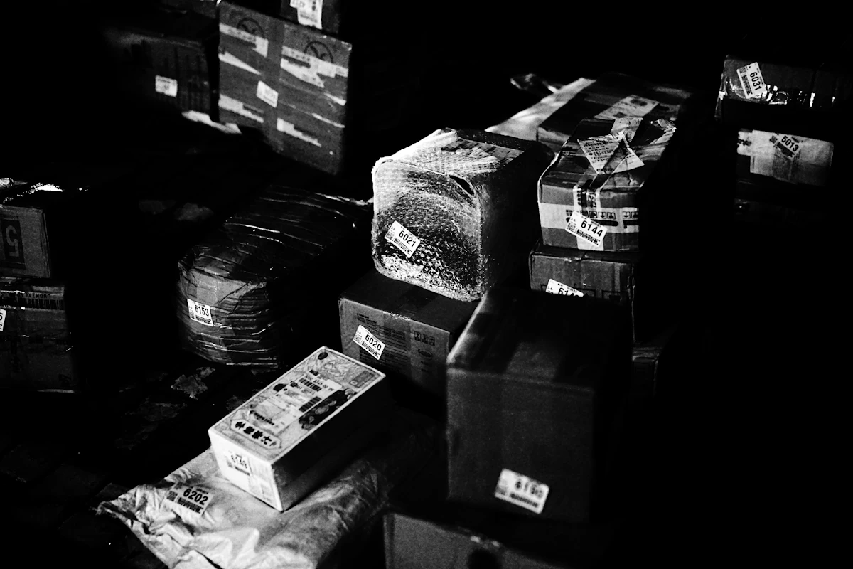 Tumpukan paket yang sudah dilakban dan berlabel di ruangan redup dengan satu lampu menyala pada malam hari