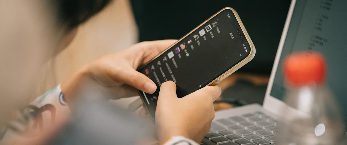 Dua tangan menggulir daftar pesan di ponsel di depan laptop terbuka