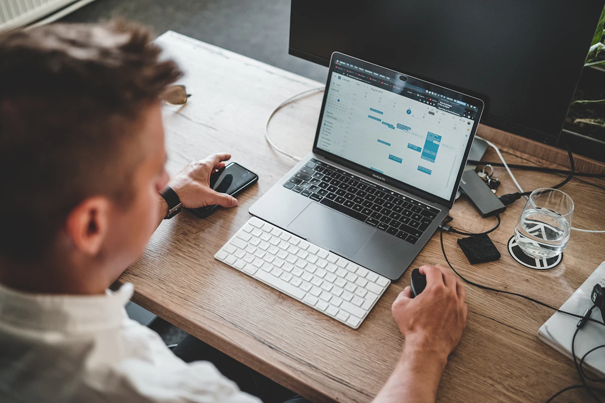 Pria bekerja di laptop dengan ponsel tergeletak di sampingnya di meja kerja