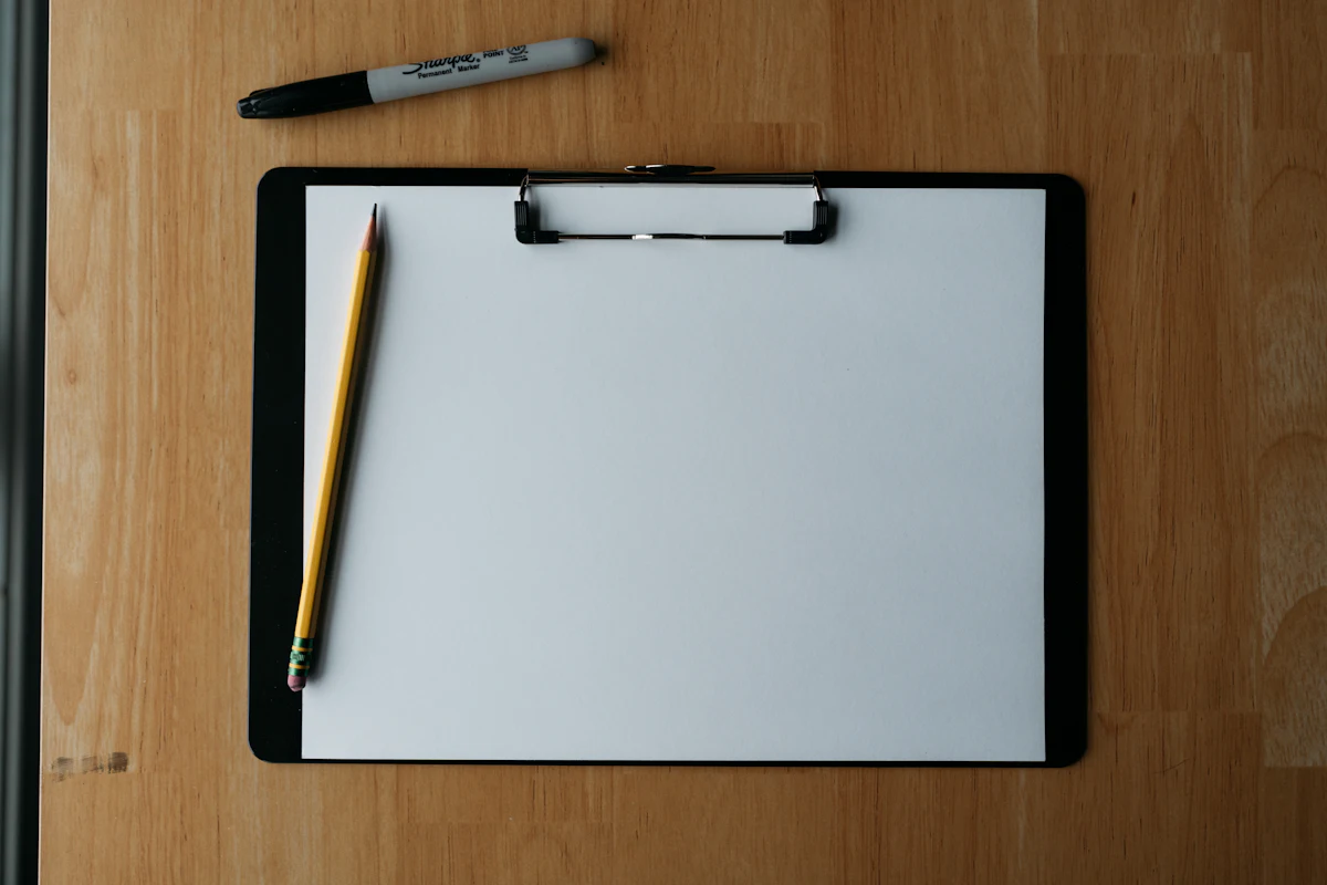 Papan jepit berisi lembar catatan dengan pulpen dan pensil di atas permukaan kayu