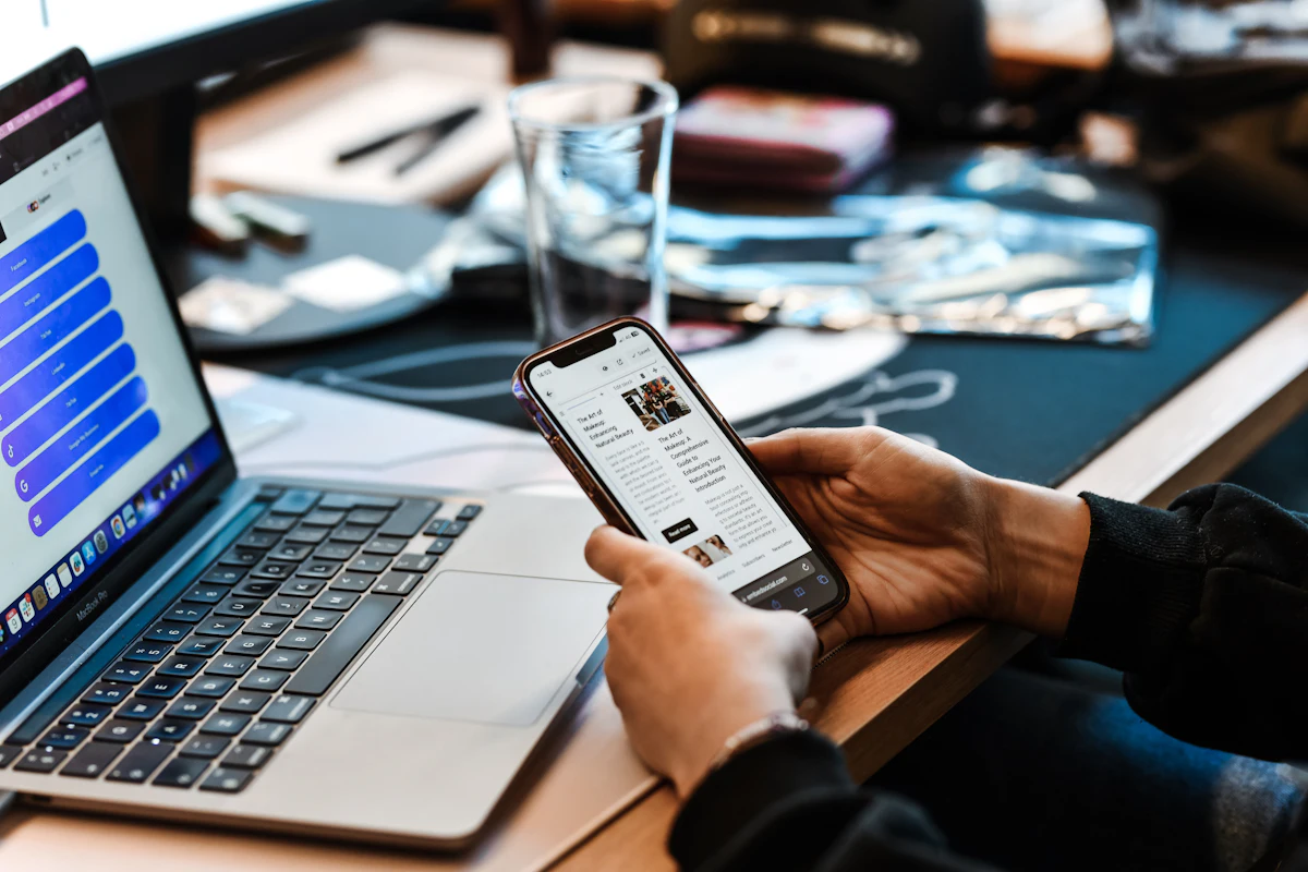 Orang memegang ponsel di meja kerja dengan laptop terbuka