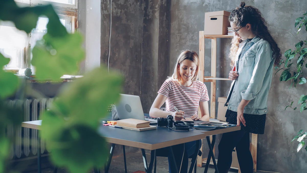 Dua perempuan bekerja berdampingan di satu meja sambil melihat layar laptop yang sama