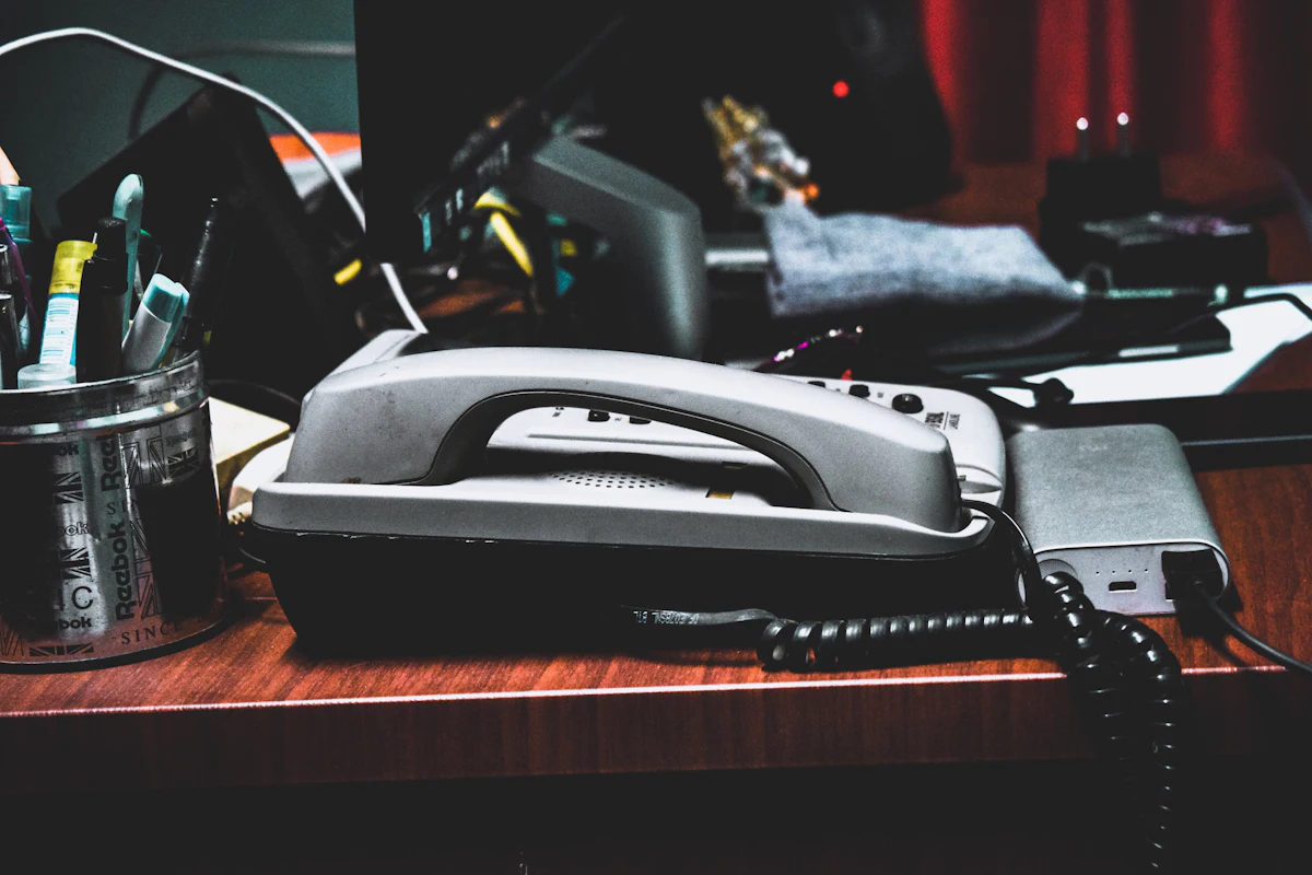 Telepon meja kantor lawas di atas meja kerja bersama pulpen dan perlengkapan tulis
