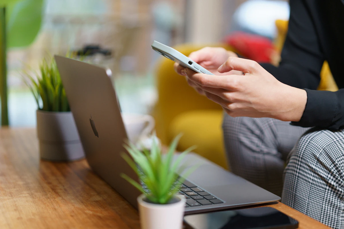 Seseorang membalas pesan di ponsel sambil duduk di depan laptop yang terbuka