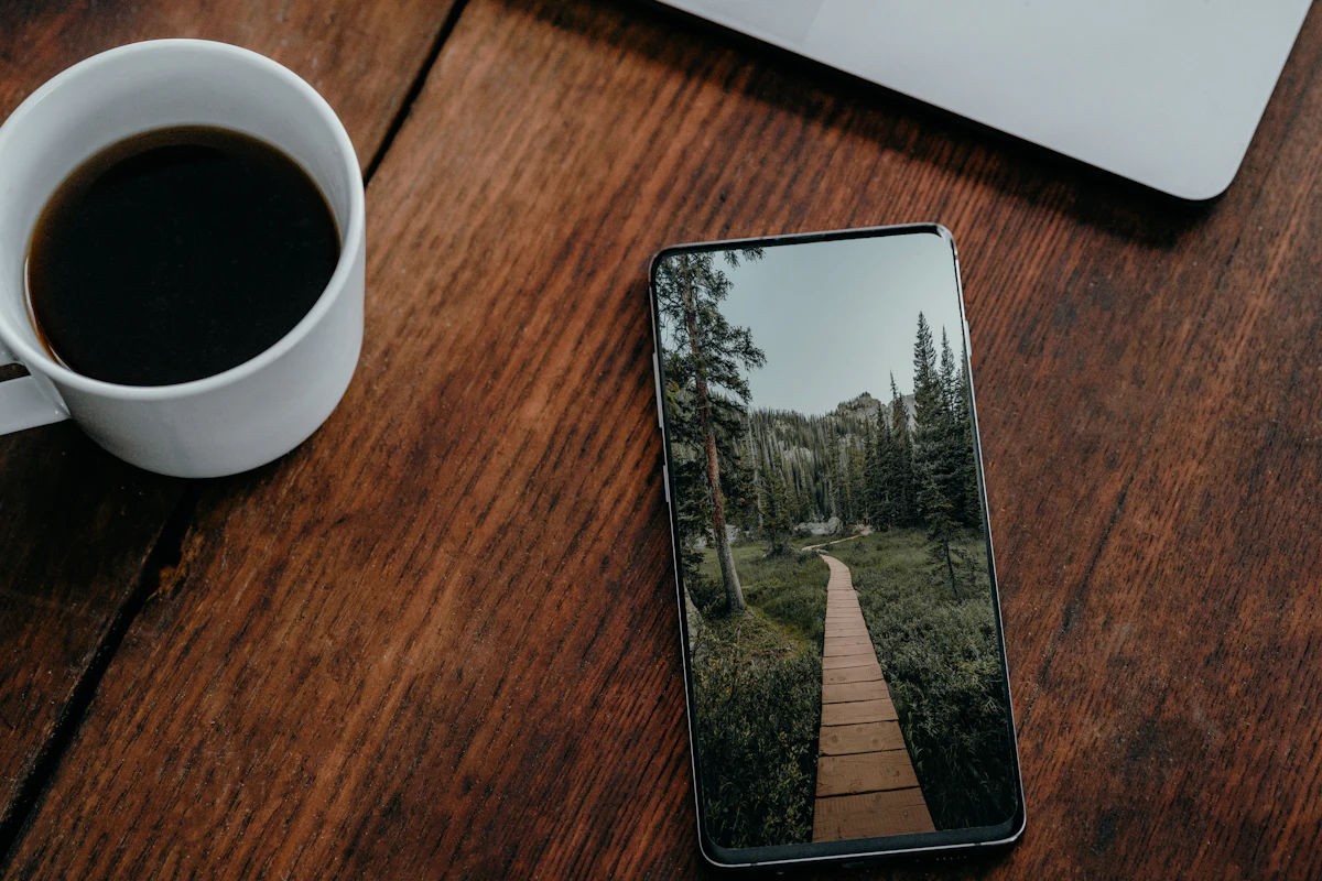 Ponsel dengan layar menyala dan secangkir kopi di atas meja kayu