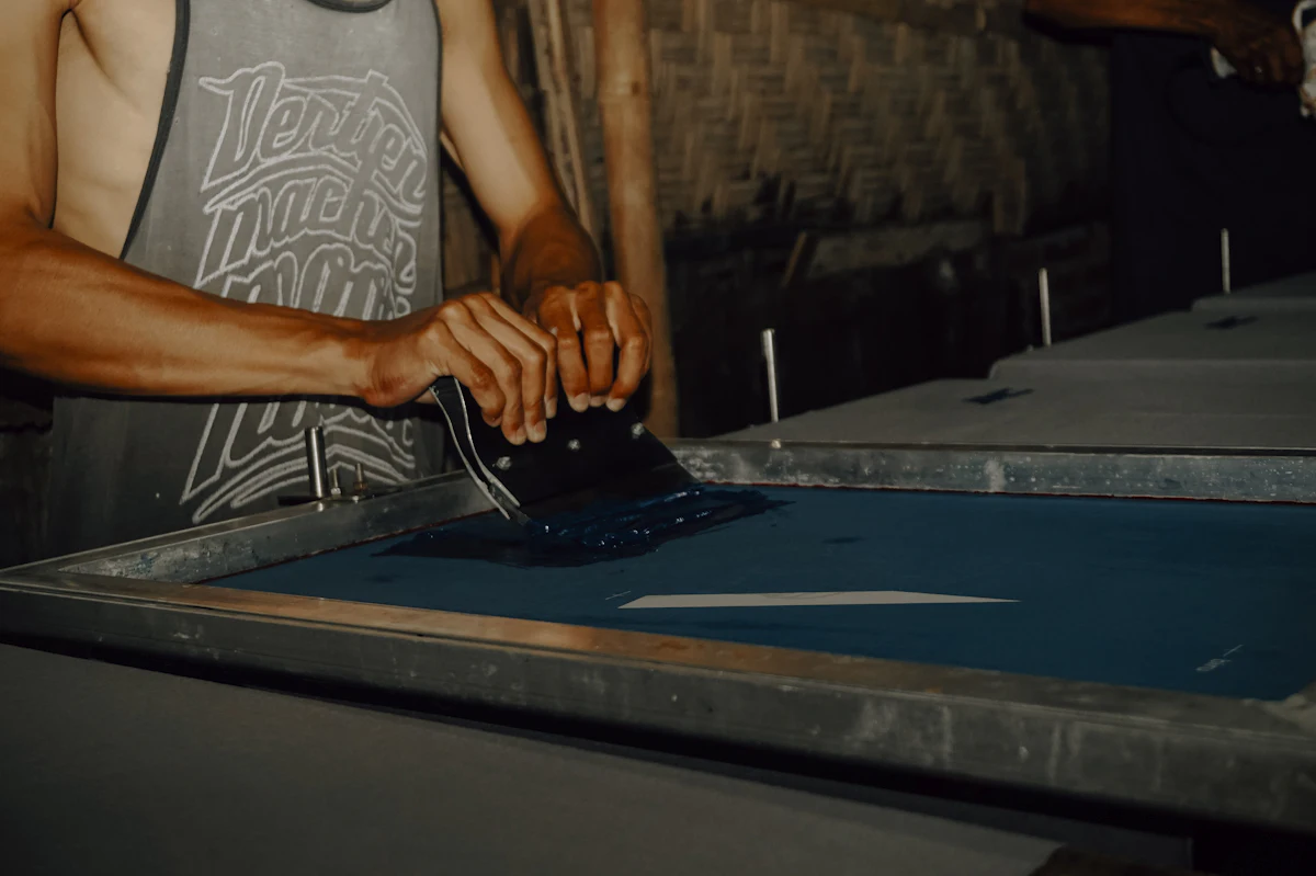 Pekerja berdiri di samping meja putar sablon manual di sebuah workshop kaos