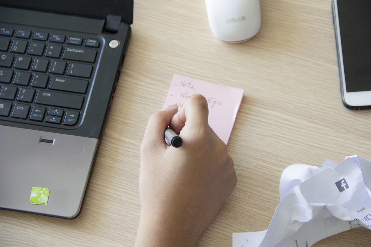 Tangan menulis di kertas catatan kecil di sebelah laptop yang terbuka