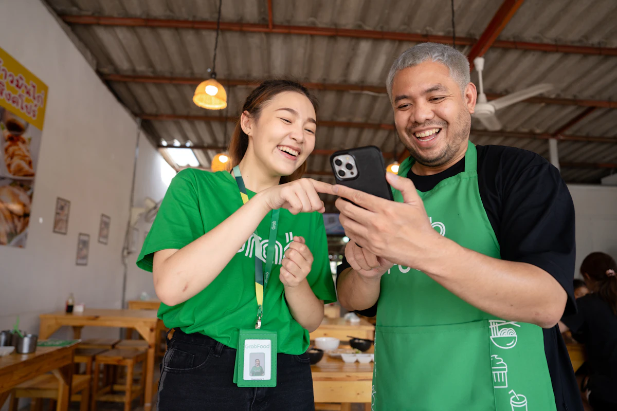 Dua staf toko berseragam apron berdiri berdampingan sambil melihat ponsel