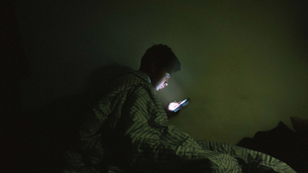 Seseorang memakai ponsel di tempat tidur pada malam hari, wajah dan selimutnya diterangi cahaya layar dalam kamar yang gelap