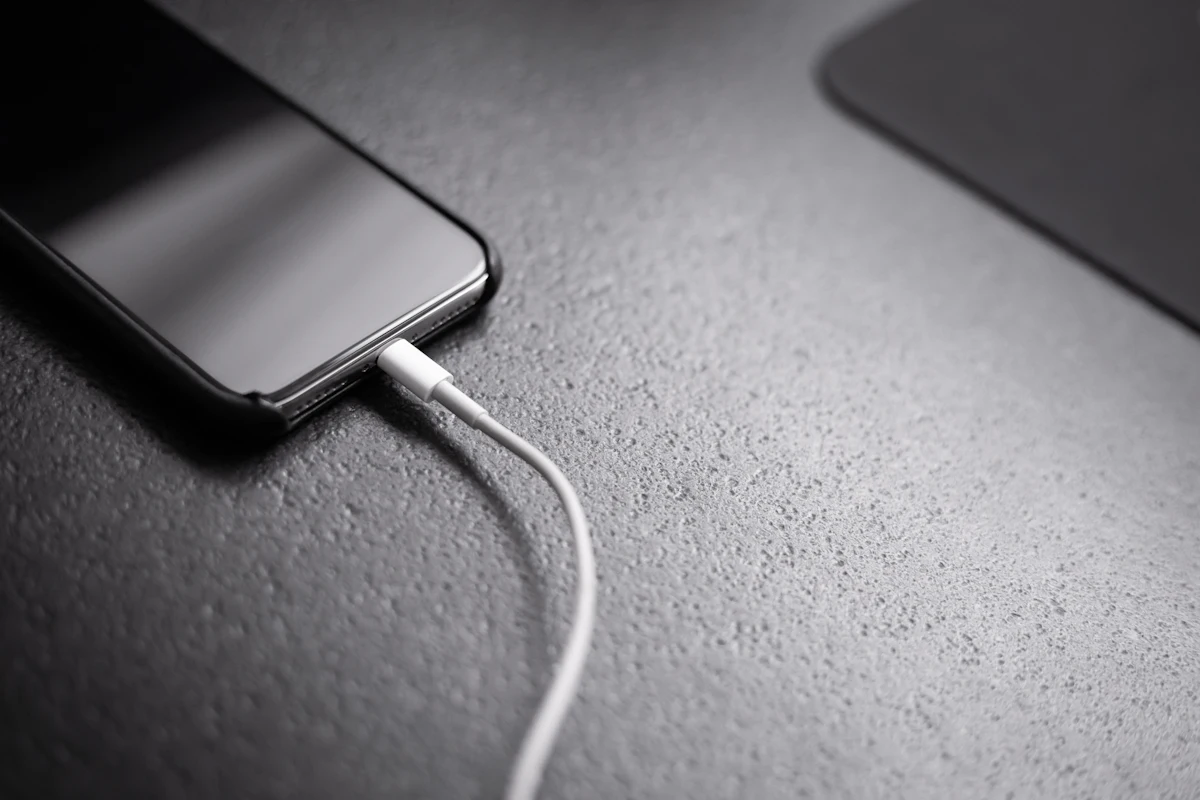 Ponsel berlayar mati tergeletak di meja dengan kabel charger di sebelahnya
