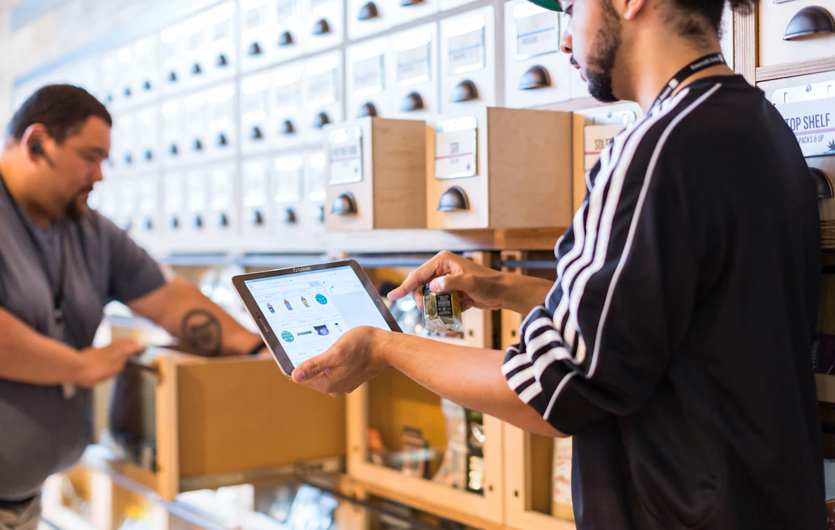 Dua staf toko memeriksa tablet di antara rak barang