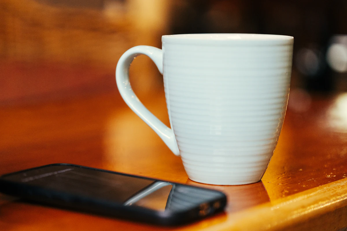 Secangkir kopi dan sebuah ponsel tergeletak di meja kayu